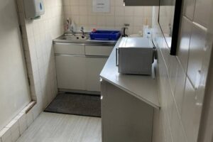 Property for sale A small kitchen in a Mansfield Road property features a sink, blue dish rack, and cleaning supplies on the worktop. A microwave sits on an angled counter, and a soap dispenser is mounted on the tiled wall. There's a mat in front of the sink. Presented by Palace Auctions