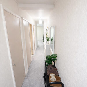 Property for sale A bright, narrow hallway welcomes you into this one-bedroom flat Nottingham, featuring beige doors on the left, a long mirror and potted plants on the right, light gray carpet, and a small black shoe rack holding shoes at the front. Presented by Palace Auctions