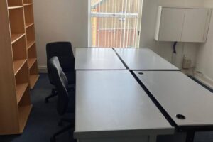 Property for sale A small office in a Mansfield Road property with four white desks pushed together, two black office chairs, a tall wooden bookcase, a wall-mounted white cupboard, and a window with vertical blinds letting in daylight. Presented by Palace Auctions