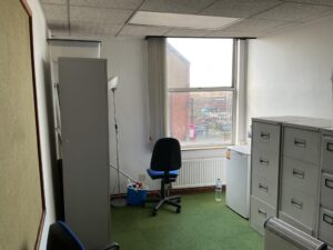 Property for sale Small office with green carpet, filing cabinets, blue chair, tall lamp, mini fridge, water bottle, and large window overlooking Mansfield Road property. Walls are mostly white with a noticeboard on the left—ideal as a development or investment property. Presented by Palace Auctions