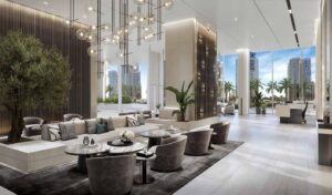 Property for sale Luxurious, modern lobby at LIV LUX with elegant seating, marble tables, a large indoor plant, hanging globe lights, and floor-to-ceiling windows offering a sea view of palm trees and Dubai Marina’s stunning skyscrapers. Presented by Palace Auctions