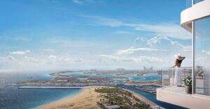 Property for sale A woman in a white dress and hat stands on the balcony of a 1BR apartment, overlooking the sea, sandy beach, and man-made islands in Dubai Marina under a bright blue sky with scattered clouds. Presented by Palace Auctions