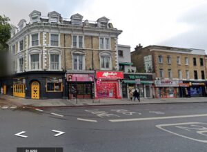 Property for sale A street view in London shows a row of shops, including a yellow restaurant, barbershop, red fast-food shop, and green convenience store set in listed townhouse buildings along a city road with a bus lane. Presented by Palace Auctions