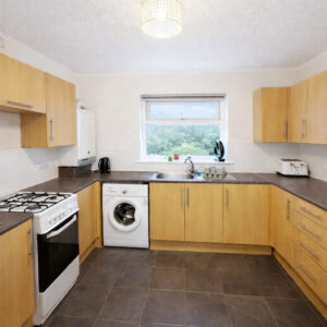 Property for sale Modern kitchen in Wynyard Mews with light wood cupboards, gas hob, washing machine, toaster, and sink under a window. Dark worktops and grey tiled floors enhance this bright, tidy space—perfect for a Hartlepool investment property. Presented by Palace Auctions