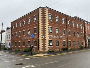 Property for sale A three-story red brick building with cream-colored accents, labeled "LOTA HEIGHTS" on two sides, stands on a street corner in Coventry. Ideal for PBSA investment, it features a pedestrian sidewalk and two people walking nearby under an overcast sky. Presented by Palace Auctions