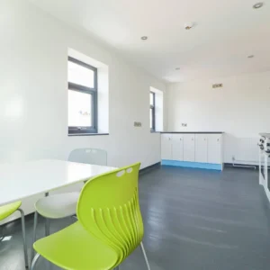 Property for sale A modern kitchen with white walls, grey flooring, green and white chairs around a table, and white cupboards beneath two windows. This bright space with natural light is an attractive feature for Coventry PBSA Investment Auction listings. Presented by Palace Auctions