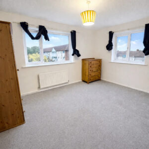 Property for sale Bright, unfurnished bedroom in Wynyard Mews with light grey carpet, cream walls, two windows with dark curtains, a wooden wardrobe, chest of drawers, and ceiling light with a yellow shade—ideal for buy-to-let investment. Houses visible outside the windows. Presented by Palace Auctions