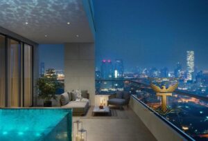 Property for sale A modern rooftop terrace at night features a pool, lounge seating, potted plants, and soft lighting, overlooking a city skyline. A gold eagle logo in the foreground hints at Ra1n Residence JVC apartment—your future Dubai investment flat 2026. Presented by Palace Auctions