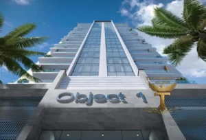 Property for sale A modern high-rise building viewed from below, with “Object 1” above the entrance. Palm trees, blue sky, and a gold “Transparency Real Estate” logo complete this Ra1n Residence JVC flat—your future Dubai investment flat 2026. Presented by Palace Auctions