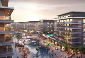 Property for sale Modern waterfront flats in DAMAC Riverside Views surround a central canal with fountains, palm trees, and outdoor seating at sunset. People stroll along the water in Dubai Investment Park 2 as “DAMAC” signage is visible on one building. Presented by Palace Auctions
