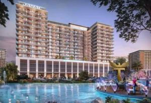 Property for sale A modern, multi-storey residential building labelled "DAMAC" overlooks a landscaped pool at sunset, offering DAMAC Riverside Views. Palm trees and people relaxing on the wooden deck highlight this stunning waterfront flat in Dubai Investment Park 2. Presented by Palace Auctions