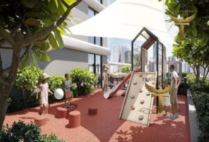 Property for sale Children play on a shaded outdoor playground with slides, climbing wall, and stepping stools, surrounded by greenery and modern buildings in Dubai’s Jumeirah Village Triangle. An adult supervises nearby under a white canopy, close to a luxury block of flats. Presented by Palace Auctions