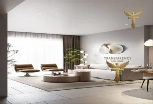 Property for sale A modern living room in a luxury flat at Jumeirah Village Triangle, Dubai, features neutral tones, two brown armchairs, a white settee, round tables, large windows with sheer curtains, and a "TRANSPARENCY REAL ESTATE" logo with a golden eagle. Presented by Palace Auctions