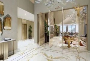 Property for sale A luxurious, modern living space in the Maldives Cluster at DAMAC Islands, featuring marble floors, gold-accented furniture, glass dividers, and large windows. Artistic décor and indoor plants enhance the elegant atmosphere of this luxury townhouse. Presented by Palace Auctions