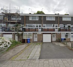 Property for sale A row of three-storey townhouses with garages, one under construction and scaffolding—ideal for those seeking an HMO investment property Derby for sale. Rubbish bins and a flowering bush sit in front beneath an overcast sky. Presented by Palace Auctions