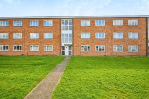 Property for sale A three-storey brick apartment building at Bembridge Place with multiple windows, a central entrance, and a pathway leading to the door, surrounded by a large green lawn under a partly cloudy sky. Presented by Palace Auctions