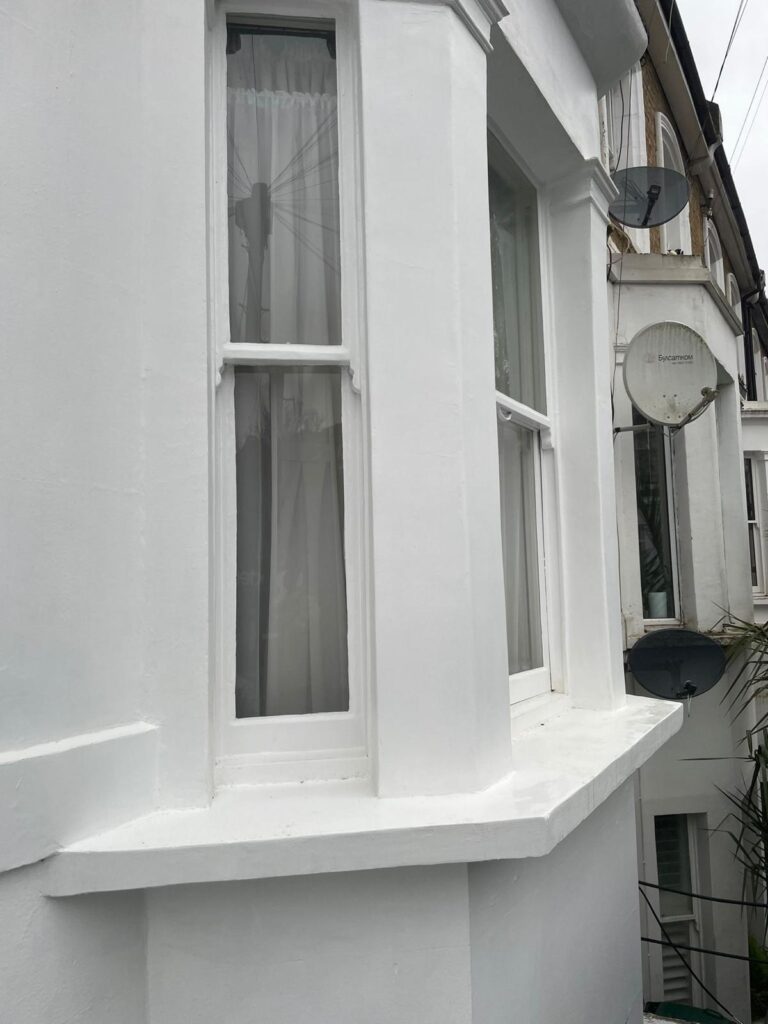 Property for sale A close-up view of a white-painted bay window on a Poets’ Corner ground floor flat with net curtains, next to a neighbouring house with satellite dishes, highlights the character of this auction property in Acton, London. Presented by Palace Auctions