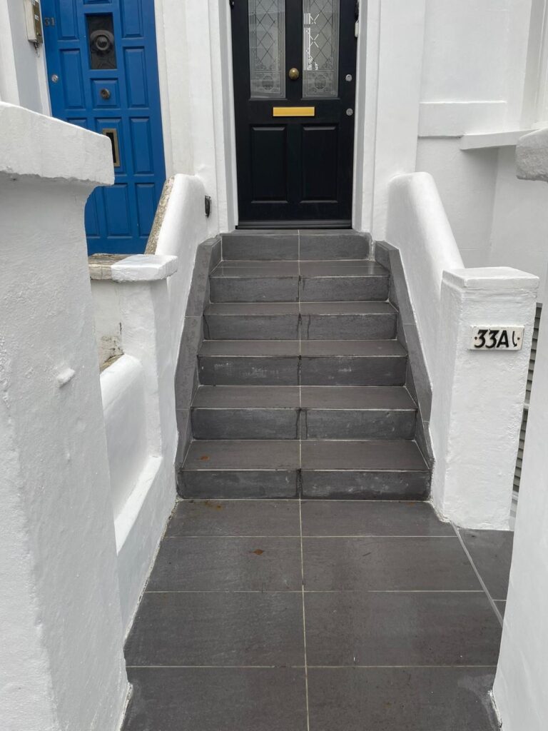 Property for sale A set of six dark grey tiled steps leads up to a black front door with glass panels and a letterbox. The door is framed by white walls, and a plaque on the right displays "33A"—perfect for an investment flat in Acton W3. Presented by Palace Auctions