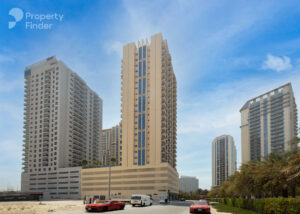 Property for sale Modern high-rise block of flats with balconies under a blue sky, seen from a street with parked and moving cars, lush greenery, and the "Property Finder" logo—ideal for your Dubai investment flat 2026 or a Luxury JVC Smart Flat. Presented by Palace Auctions