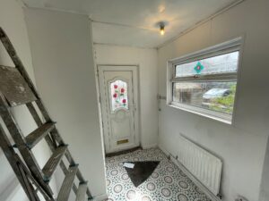 Property for sale A cosy entrance hall in this Stanley 3-bed terrace features a patterned tiled floor, white walls, a ladder leaning on the left, a white front door with decorative glass, a window above a radiator, and sunlight streaming through. Presented by Palace Auctions