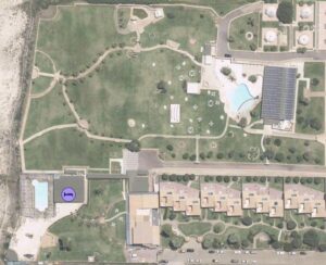 Property for sale Aerial view of a resort with a large green lawn, a swimming pool on the left, a solar panel-covered building and pool on the right, and several rows of tan buildings at the bottom. A purple wheelchair icon marks pool access. Presented by Palace Auctions