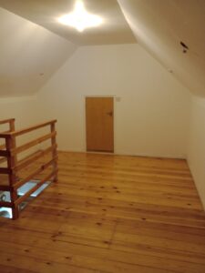 Property for sale A small attic room with sloping white walls, wooden floorboards, a wooden bannister on the left overlooking stairs, and a short wooden door on the far wall. The room is lit by a ceiling light. Presented by Palace Auctions