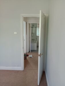 Property for sale A white door is partially open, revealing a beige carpeted room and a bathroom with a glass shower. Cleaning supplies and cloths are scattered on the floor near the doorway. Presented by Palace Auctions