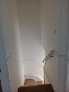 Property for sale A narrow, carpeted stairway with white walls and a silver handrail curves to the left and descends out of view, lit by natural or overhead light. The walls have decorative moulding. Presented by Palace Auctions