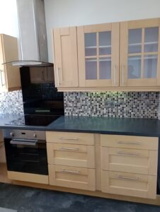 Property for sale Modern kitchen with light wood cupboards, a black worktop, mosaic tile splashback, an electric oven with a hob, and a stainless steel extractor hood. Upper cupboards have frosted glass panels. Presented by Palace Auctions