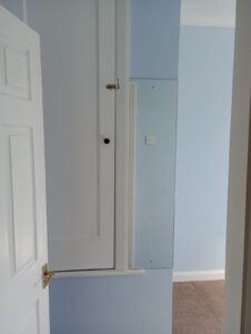 Property for sale A white door opens into a light blue room with a white cupboard fitted high on the wall and a tall, narrow mirror or panel next to it above a section of brown carpet. Presented by Palace Auctions