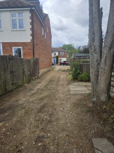 Property for sale A dirt alleyway runs between two wooden fences beside a brick house—perhaps reminiscent of an auction property in Dartford—leading to a residential street with parked cars and more houses visible under a cloudy sky. Presented by Palace Auctions
