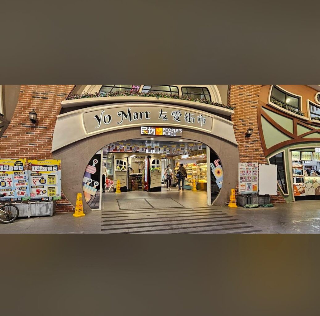 Property for sale Entrance of Yo Mart, a convenience shop with a sign reading “People’s Place.” The arched doorway, brick walls, and warm lighting create a welcoming vibe—perfect for those exploring Buy-to-let Hong Kong opportunities nearby. Presented by Palace Auctions