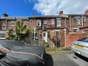 Property for sale A row of brick terraced houses with chimneys, a small fenced front garden, a tree, and two parked cars—one covered—sits beneath a blue sky. Classic Stanley residential property, ideal for those seeking a County Durham house auction opportunity. Presented by Palace Auctions