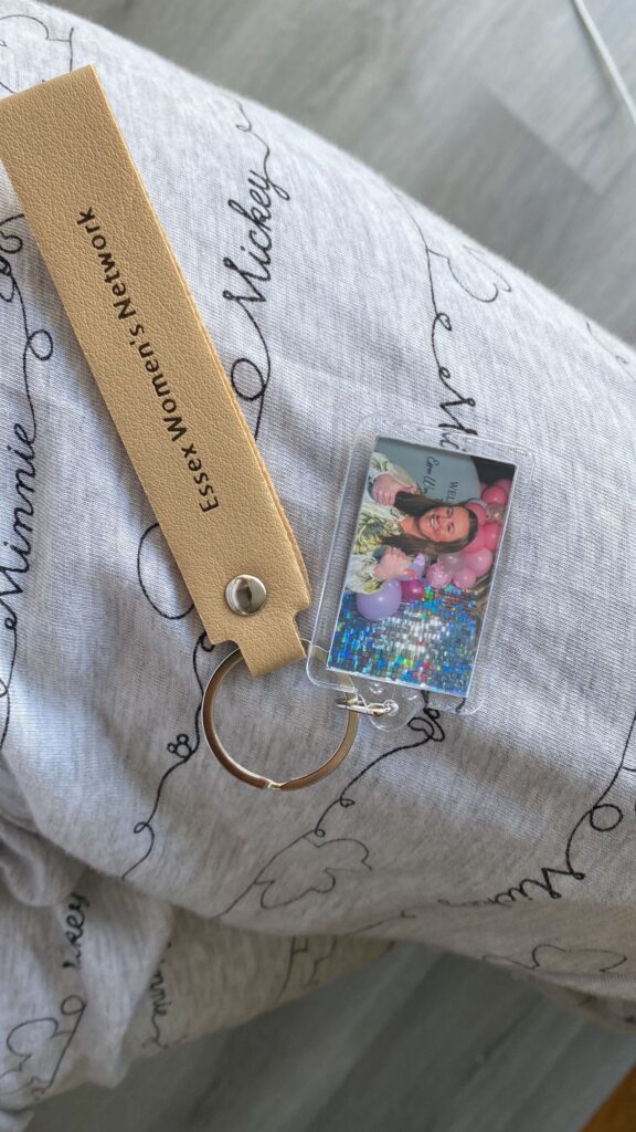Property for sale A tan leather keyring with "Essex Women’s Network" printed on it lies on grey fabric with "Minnie" and "Mickey" in cursive. This Founders’ Edition keyring features a photo of a woman smiling among pink balloons, celebrating the Launch Event. Presented by Palace Auctions