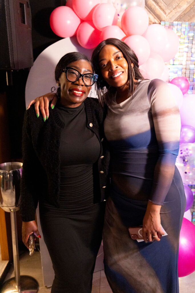 Property for sale Two women smiling and posing together at the Essex Women’s Network Founders Edition Launch Event, one wearing glasses and a black outfit, the other in a grey dress, with pink and purple balloons in the background. Presented by Palace Auctions