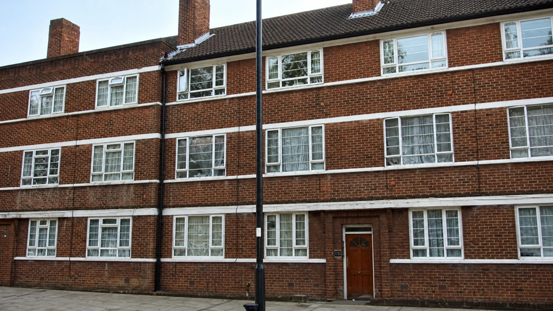 Property for sale A brick block of flats with white-trimmed windows, three storeys high, and a brown front door. A black streetlamp stands on the paved pavement in front of this appealing Harrow investment flat. Presented by Palace Auctions