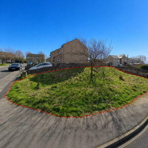 Property for sale A grassy, sloping Freehold Building Plot in Ingleton, North Yorkshire, bordered by a red outline, nestled between a pavement and two residential streets with houses, parked cars, and leafless trees under a clear blue sky. Presented by Palace Auctions