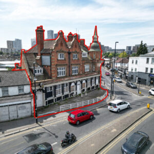Property for sale A large, old red-brick building with white-trimmed windows—ideal for Croydon mixed use investment—is outlined in red beside a curved street with cars and a motorbike passing by. Modern buildings rise in the background under a partly cloudy sky. Presented by Palace Auctions