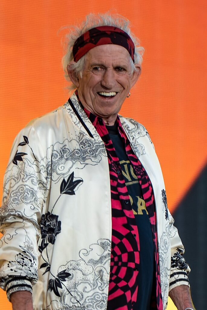 Property for sale An older man with white hair, wearing a patterned headband, a white floral jacket, and a dark graphic shirt, smiles in front of an orange background—reflecting the client-focussed auctioneers behind leading probate and land sales. Presented by Palace Auctions