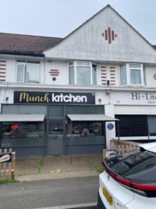 Property for sale A white building with a "Munch Kitchen" café sign above large windows. Menu items—breakfast, cakes, coffee—are displayed on the glass. A parked white car is in front, highlighting its prime location near client-focussed auctioneers and probate and land sales services. Presented by Palace Auctions