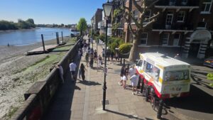 Property for sale People stroll along Clavering Avenue SW13 on a sunny day, passing an ice cream van beside historic brick buildings; the river and its exposed muddy banks are visible to the left. Presented by Palace Auctions