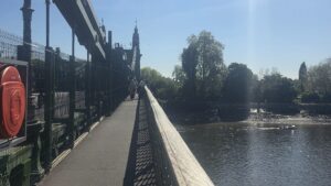 Property for sale People walk across a bridge on a sunny day beside a calm river in SW13; trees line the far bank near Clavering Avenue, and a small boat floats on the water. Presented by Palace Auctions