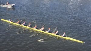 Property for sale A team of eight rowers and a cox glides in a yellow racing shell on a river near Clavering Avenue, SW13, with a small motorboat nearby on the left side of the image. Presented by Palace Auctions