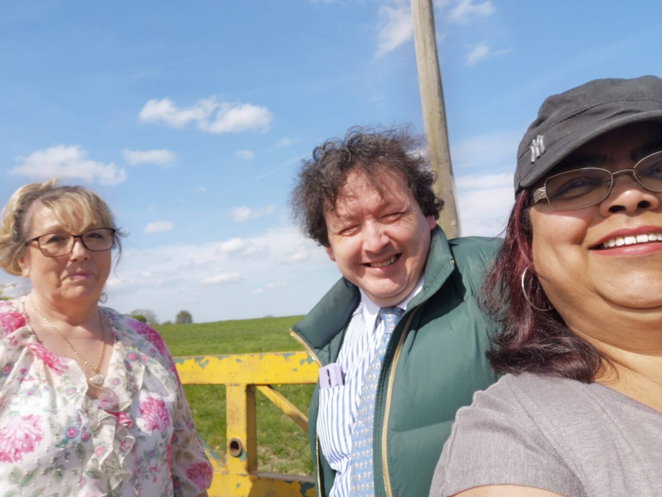 Property for sale Three adults stand outside on a sunny day in front of a yellow gate with green fields and blue sky behind them, reflecting the friendly, client-focused auctioneers at Palace Auctions Bank Holiday—experts in probate and land sales. Presented by Palace Auctions