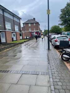 Property for sale A wet pavement lined with parked cars on the right and brick buildings on the left. A few people walk in the distance under a cloudy sky, while trees and streetlights line the road. Presented by Palace Auctions