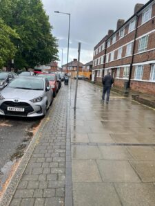 Property for sale A wet city pavement with parked cars on the left and a person walking away on the right. Brick blocks of flats line the street, and the sky is overcast. Presented by Palace Auctions