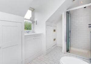 Property for sale A bright, white bathroom with sloped ceilings, a glass-enclosed shower, tiled floor, small window, and built-in cupboards beneath the window. Presented by Palace Auctions