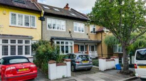 Property for sale A residential street with two cars parked in front of terraced houses. The houses have brick exteriors, large windows, and tiled roofs. A tree stands on the pavement beside the parked cars. Presented by Palace Auctions