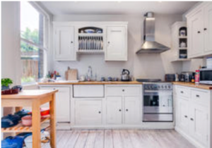 Property for sale Bright kitchen with white cupboards, wooden worktops, a modern cooker with a metal hood, open shelves, and a large window letting in natural light. A wooden island with plants and kitchen items is in the foreground. Presented by Palace Auctions