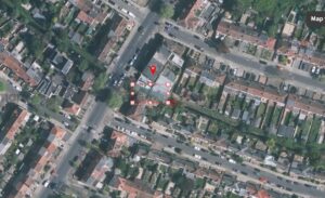 Property for sale Aerial view of a residential neighbourhood in Lambeth with rows of houses, gardens, and streets. A red location pin and blue-dotted boundary highlight a land parcel near the centre. Trees line roads, properties, and the nearby river bank. Presented by Palace Auctions